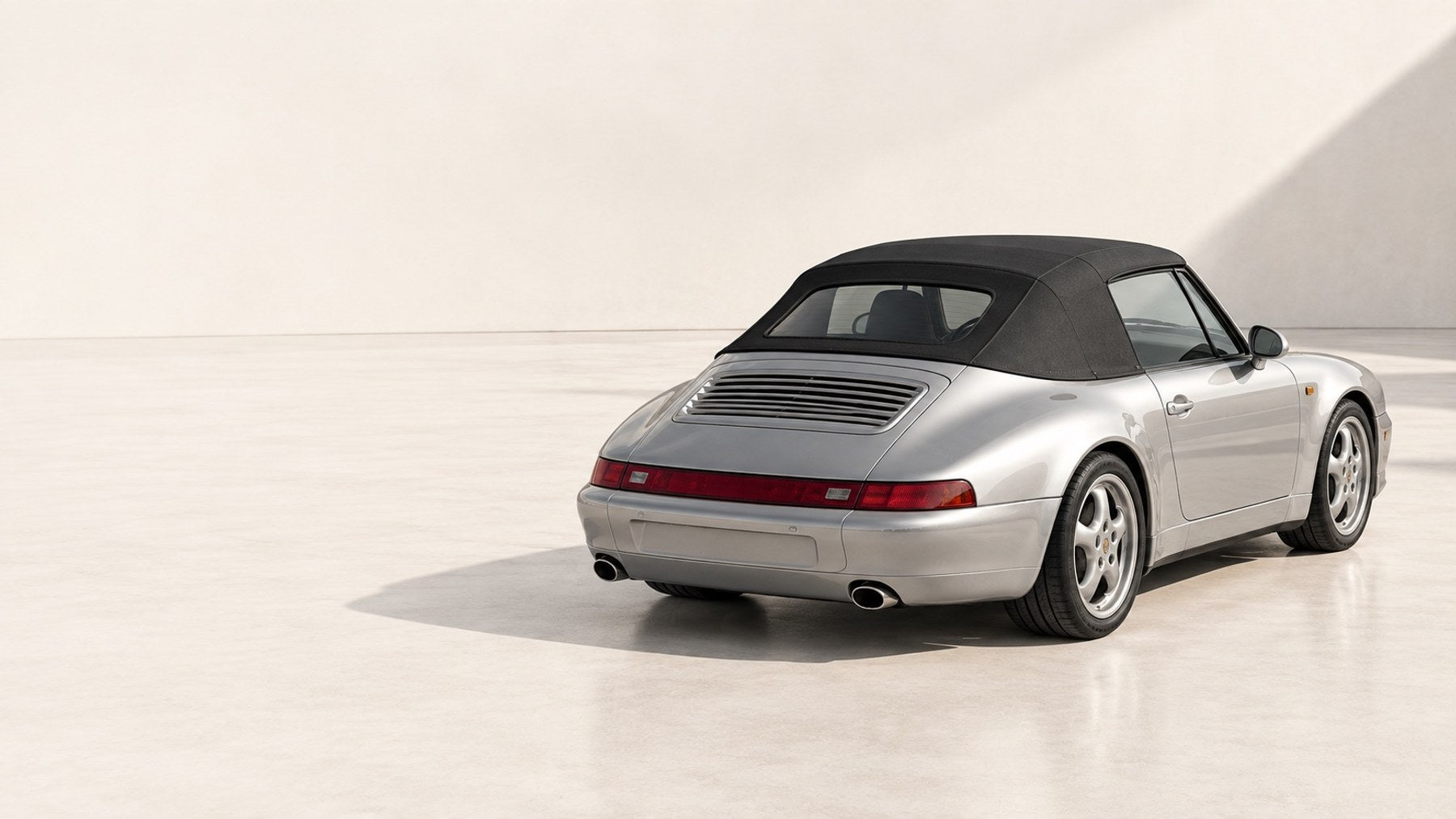 Porsche 911 cabriolet argent, capote noire fermée, vue de trois quarts arrière